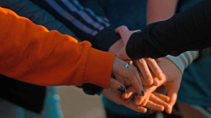 Eine Gruppe Jugendliche steht im Kreis und legt die Hände in der Mitte übereinander